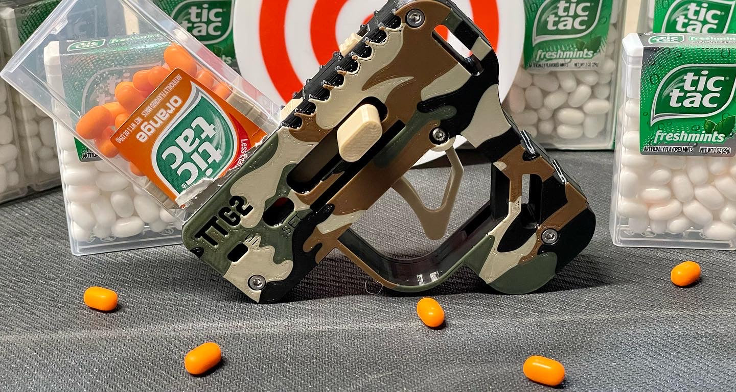 Camouflage Tic Tac Gun with Tic Tac mints on a gray surface
